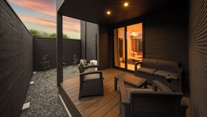 An outdoor patio with wicker furniture, a wooden deck, and a view of the sunset through large sliding glass doors.
