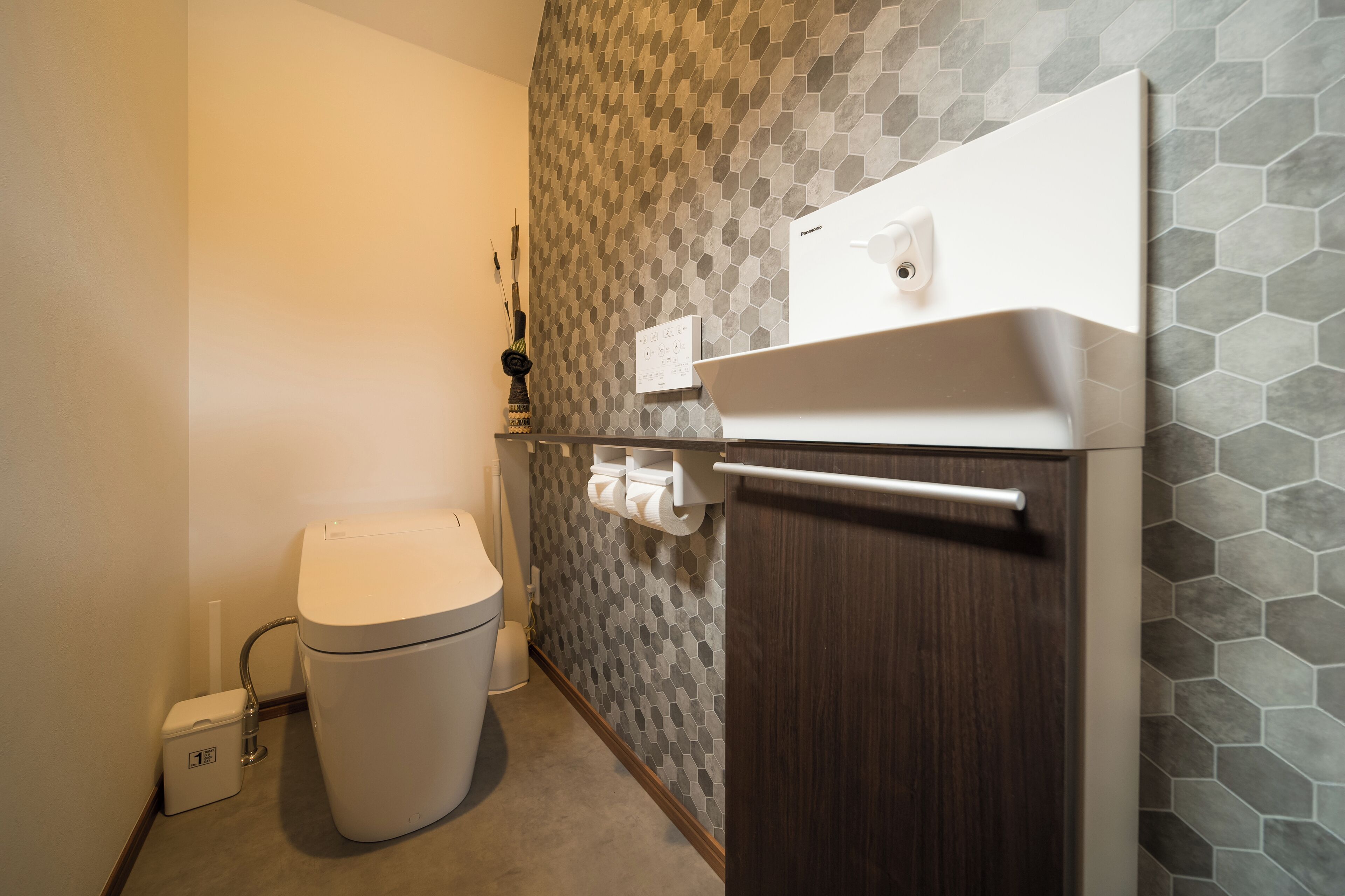 Ein Badezimmer mit Toilette, einem Mülleimer, einem Handtuchhalter und einer Wand mit sechseckigen Fliesen.