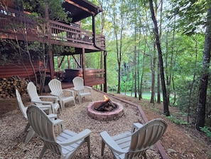 A deck with Adirondack chairs, a fire pit, and a wooden cabin in a forest.