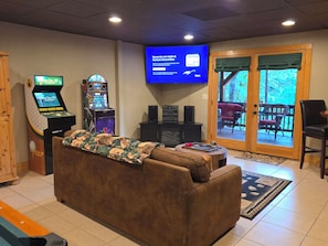 A living room with a couch, a television mounted on the wall, and two arcade games.