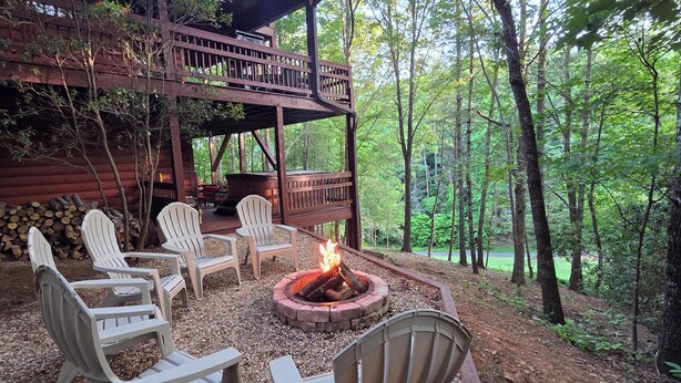 A wooden deck with Adirondack chairs, a fire pit, and a log stack.