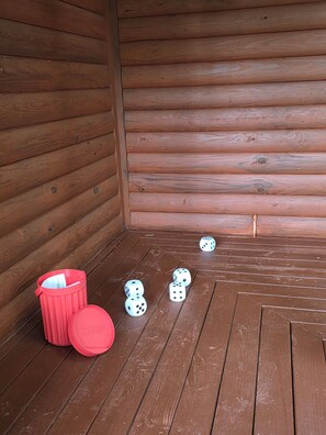 A wooden cabin interior with a red trash bin and dice on the floor.
