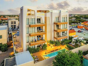 Un hotel moderno con varios balcones, piscina y vistas del entorno.