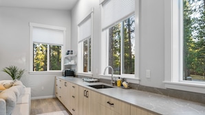A modern kitchen with a large island, white cabinetry, and a view of trees through the windows. - House+ADU+GameRoom+Jacuzzi+Pool+Fire pit+Loft (Sisters)