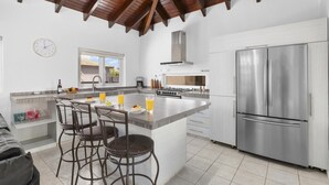 A modern kitchen with a large island, stainless steel appliances, and a dining area with wicker chairs.