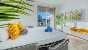 A modern hotel room with a bed, a TV, and a balcony with a view of buildings.