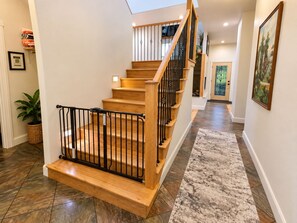 Un escalier en bois avec des rampes noires menant à l’étage supérieur, un tapis à motifs sur le sol et une porte au fond du couloir.