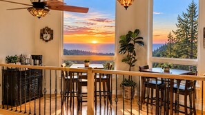 A dining area with a view of the sunset over the ocean, a ceiling fan, and a coffee station.