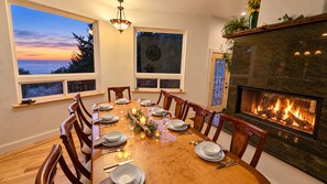 Une salle à manger avec une grande table dressée pour six personnes, bordée de fenêtres et agrémentée d’une cheminée.