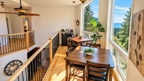 A dining area with a wooden table and chairs, a coffee machine, and a view of the outdoors through large windows. - Mountain Azure Shelter Cove - Lost Coast Ocean View, Sleeps 16, Retreats (Whitethorn)