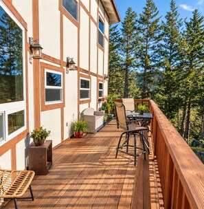 Eine Holzterrasse mit Gartenmöbeln, Topfpflanzen und Blick auf ein bewaldetes Gebiet.