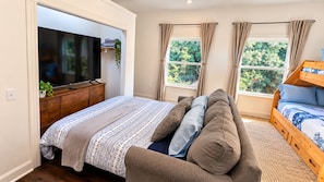 A bedroom with a bed, a wooden dresser, a TV, and a window with curtains.