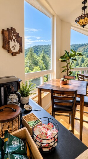 A dining area with a view of a forest, a coffee maker, and a plant on the table. - Mountain Azure Shelter Cove - Lost Coast Ocean View, Sleeps 16, Retreats (Whitethorn)