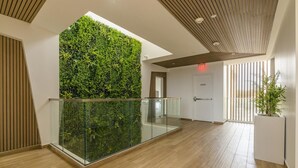 Un intérieur moderne avec une balustrade en verre donnant sur un mur végétal luxuriant, un plancher en bois et un plafond orné de lambris en bois disposés en lignes.