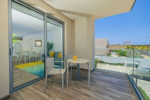A balcony with a glass door leading to a dining area, a small table with a glass of orange juice, and a view of the street and buildings.