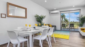 A modern dining area with a white table, white chairs, and a yellow rug. - ⁠Amazing 2BR Condo w/ Gym & Pool in Prime Location (Palm Beach)
