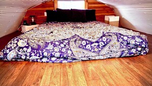 A bedroom with a sloped ceiling, a bed with a patterned bedspread, a bedside table, and a window.