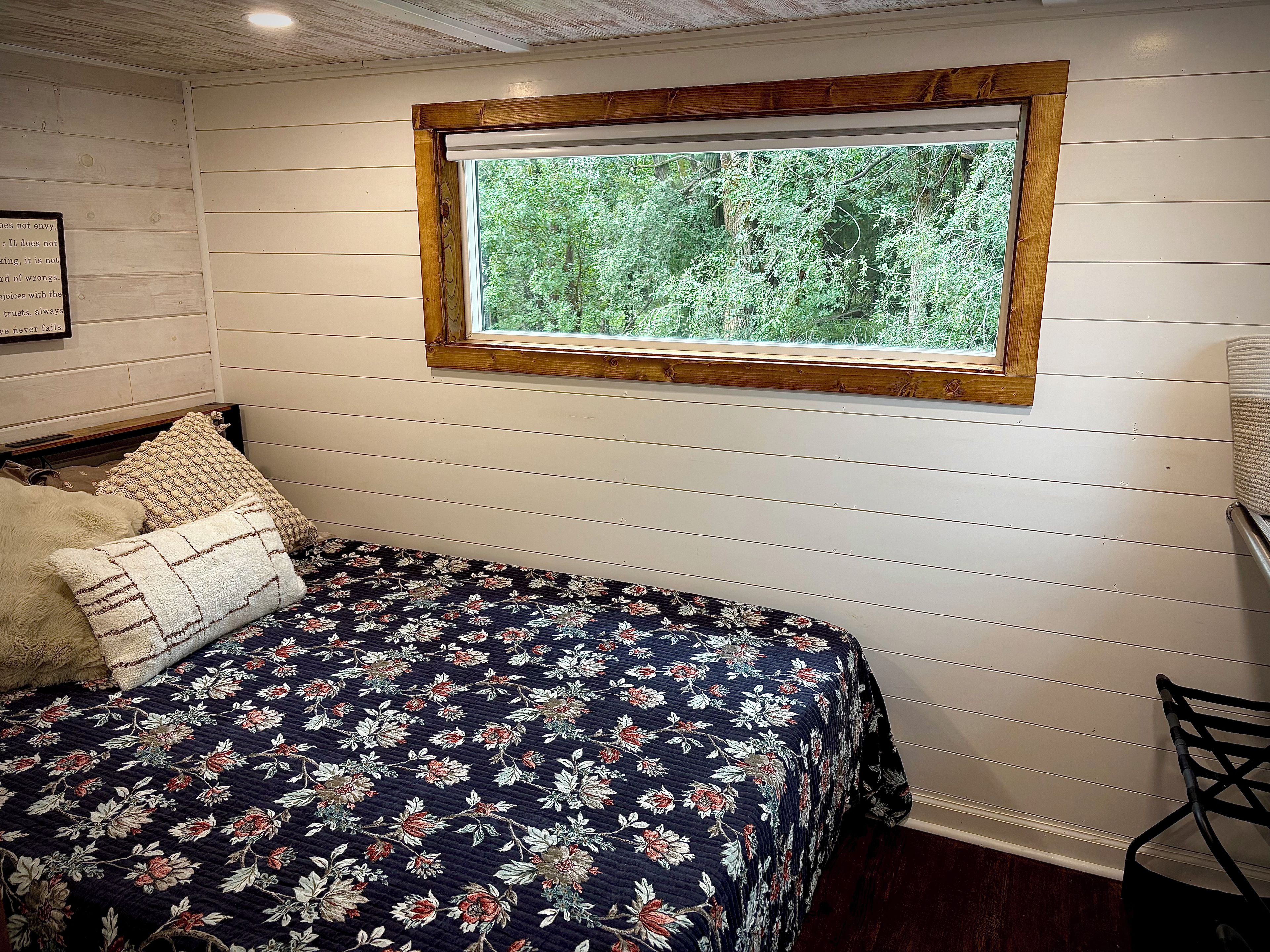 A room with a bed, a window with a view of greenery, and a wooden headboard.