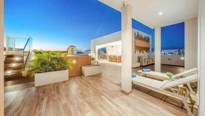 A spacious rooftop lounge with a wooden floor, seating areas, and a view of the cityscape.