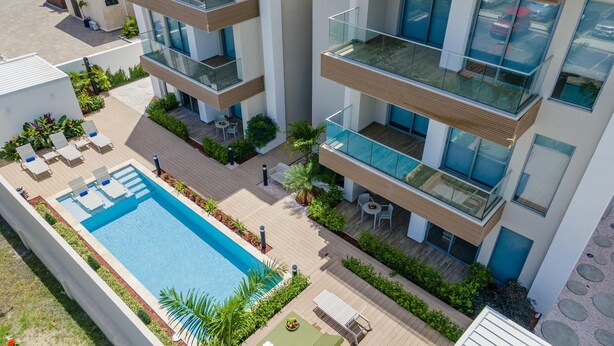 A modern apartment building with a rooftop pool, outdoor seating, and lush landscaping.