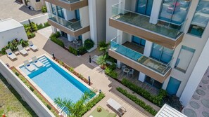 Un moderno edificio de apartamentos con piscina en la azotea, mobiliario exterior y exuberante jardinería.