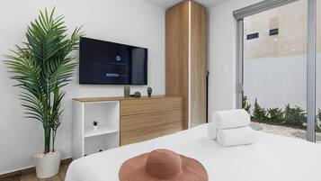 Une chambre d’hôtel moderne avec un grand lit, un téléviseur fixé au mur, une armoire en bois et une plante en pot.