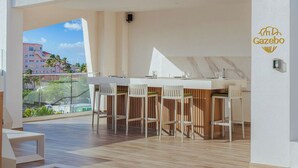 A modern outdoor bar area with a white countertop and wooden chairs, overlooking a cityscape. - NEW 2BR Condo  Pool, Gym, & Steps from Palm Beach (Palm Beach)