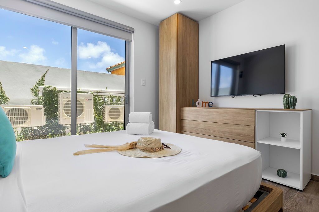 Ett modernt hotellrum med en stor säng, en platt-TV som är monterad på väggen och utsikt över stadsbilden genom stora fönster.