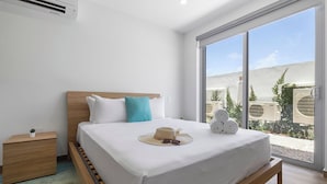 Un dormitorio con cama, una mesita de noche, un ventanal con vistas a la vegetación y un equipo de aire acondicionado.