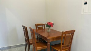 Un comedor con una mesa de madera y cuatro sillas, un florero con flores y un interruptor de luz en la pared.