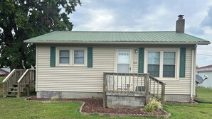 Een gelijkvloers huis met een groen metalen dak, een veranda met een kleine trap en het nummer '6314' op de deur.