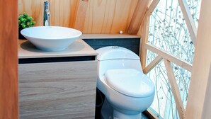 Un baño de madera pequeño y acogedor, con un lavamanos y un inodoro blancos, y una ventana con marco de madera.