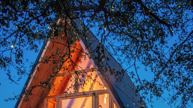 Una cabaña de madera acogedora, de forma triangular, con una puerta de vidrio que da a una cama y un jacuzzi pequeño.