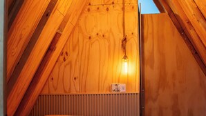 Un dormitorio acogedor en el ático, con techo inclinado, paredes de madera, una cama y una lámpara colgante.