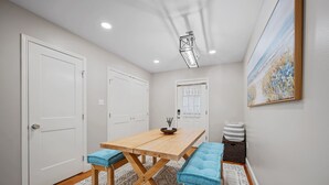 A dining area with a wooden table and blue cushioned benches, white doors, and a patterned rug.