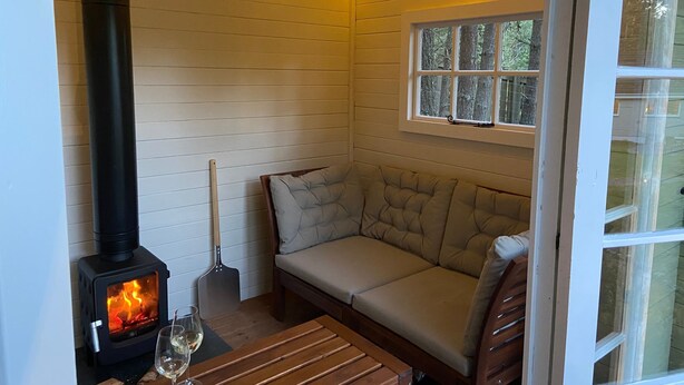 A cozy room with a wood-burning stove, a cushioned bench, and a table with glasses. - Mallard - sleeps 6 guests in 3 bedrooms (Boat of Garten)