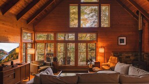 Un interior de cabaña acogedor, con detalles de madera, ventanas amplias, chimenea y televisor.