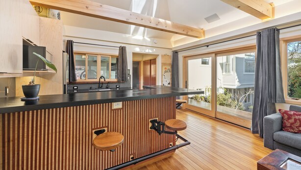 A modern kitchen with a wooden island, bar stools, and a large window offering a view of the outdoors.
