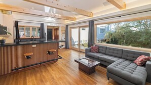 A spacious living area with a wooden floor, a grey sofa, a coffee table, and a large window offering a view of the outdoors.