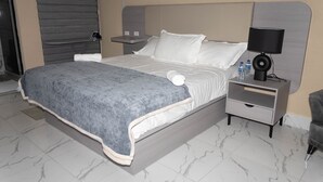 A hotel room with a bed, a nightstand, a lamp, and a chair. - CROWN HOTEL GUYANA INC (Georgetown)