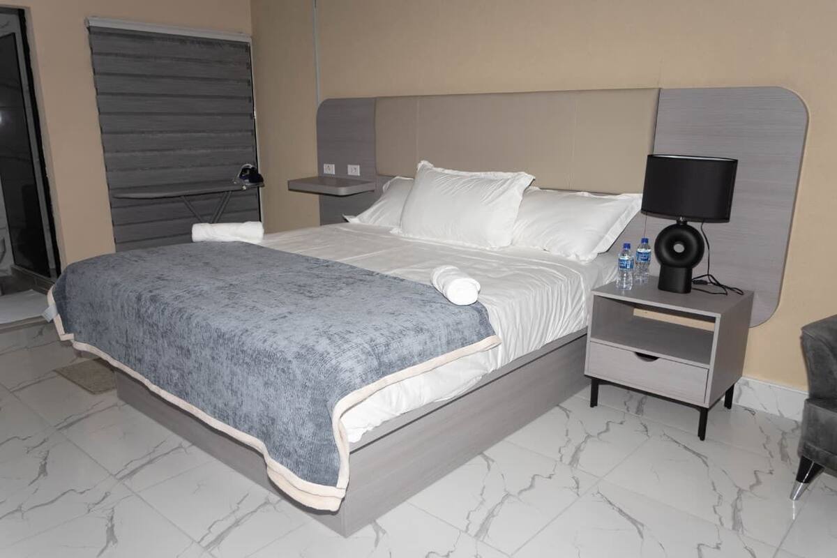 A hotel room with a bed, a nightstand, a lamp, and a chair.
