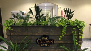 A wooden reception desk with the sign "Crown Hotel" and a crown logo. There are potted plants on either side of the desk. - CROWN HOTEL GUYANA INC (Georgetown)