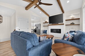 A modern living room with a sofa set, a wooden coffee table, a flat-screen TV mounted on the wall, and a ceiling fan.