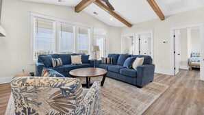 A spacious living room with a large blue sectional sofa, a round coffee table, and a ceiling fan. - Brand New 7 Bedroom, 7 Bathroom Beach House (Ocean Isle Beach)