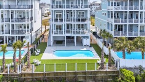 A multi-story residential building with balconies, a swimming pool, and a well-maintained lawn. - Brand New 7 Bedroom, 7 Bathroom Beach House (Ocean Isle Beach)