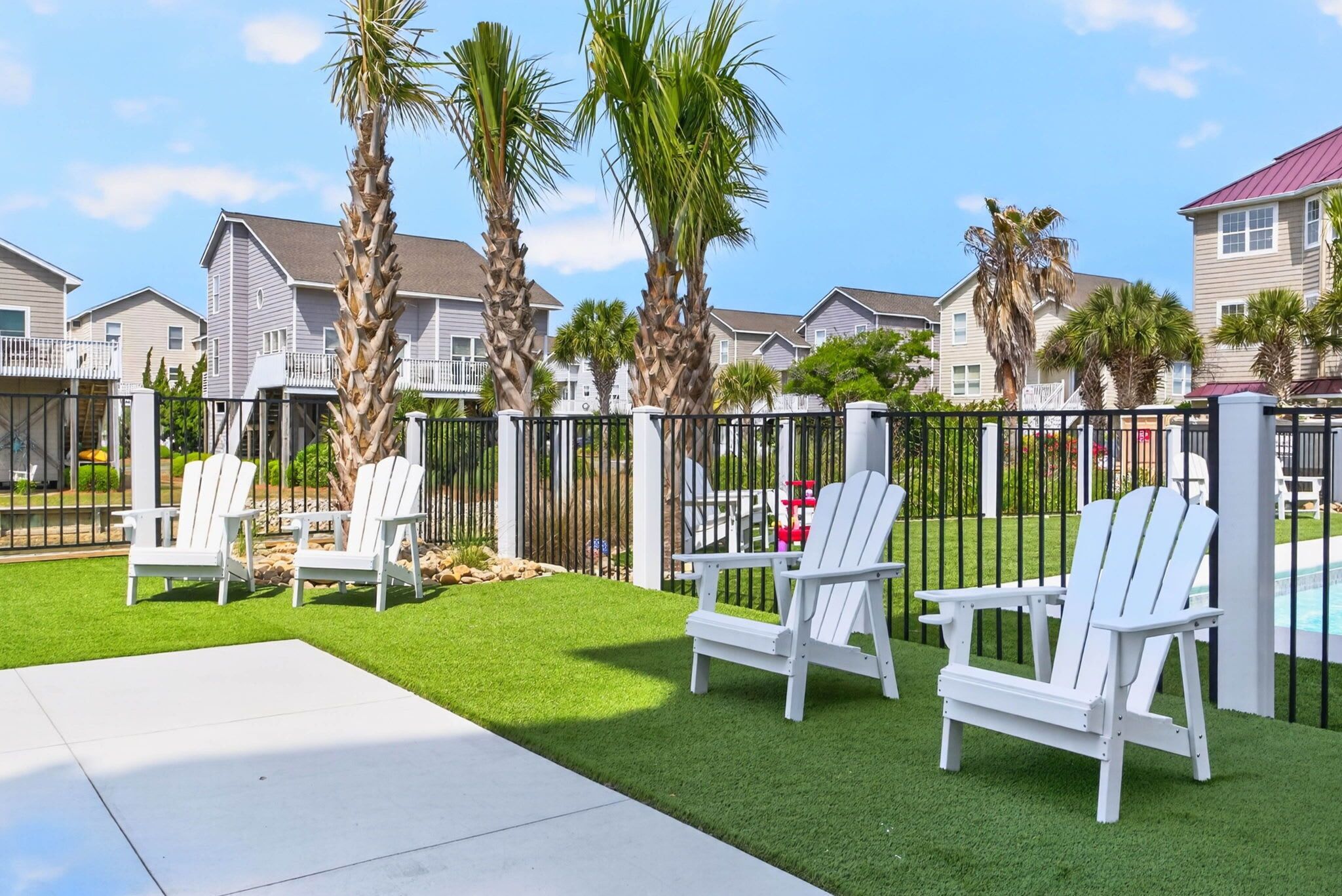 Zona residencial con casas, un patio cercado y sillas Adirondack blancas.