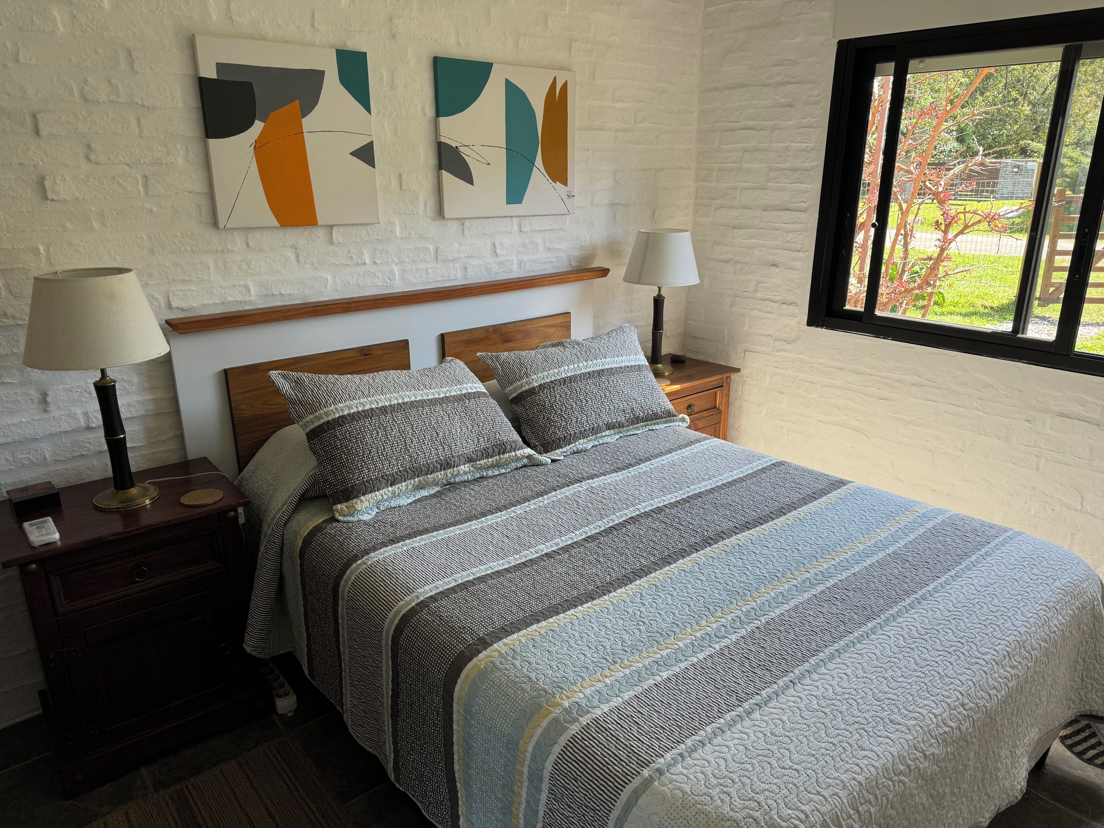 A bedroom with a bed, two bedside tables, a window, and abstract wall art.