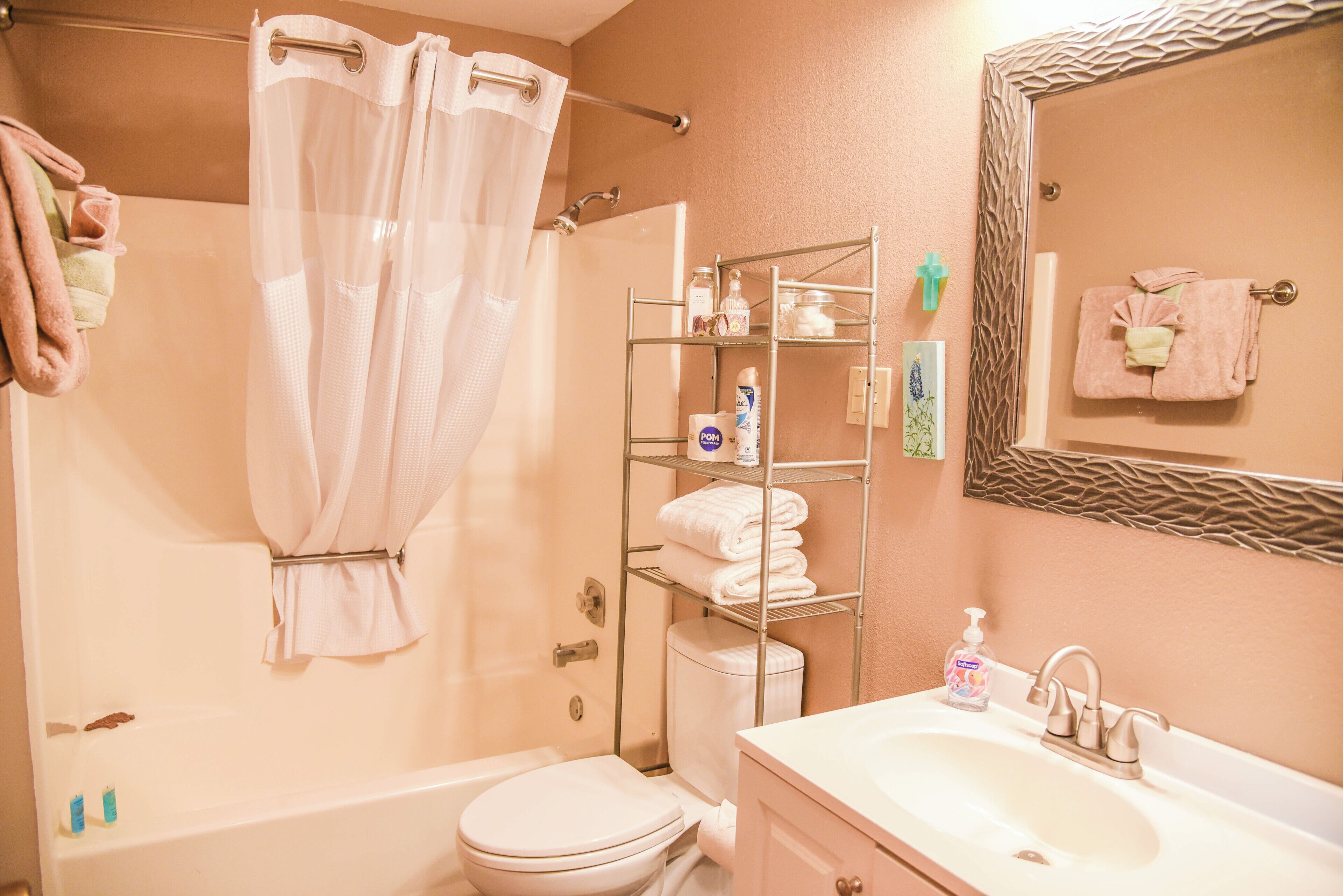 A bathroom with a shower, toilet, sink, and a towel rack.