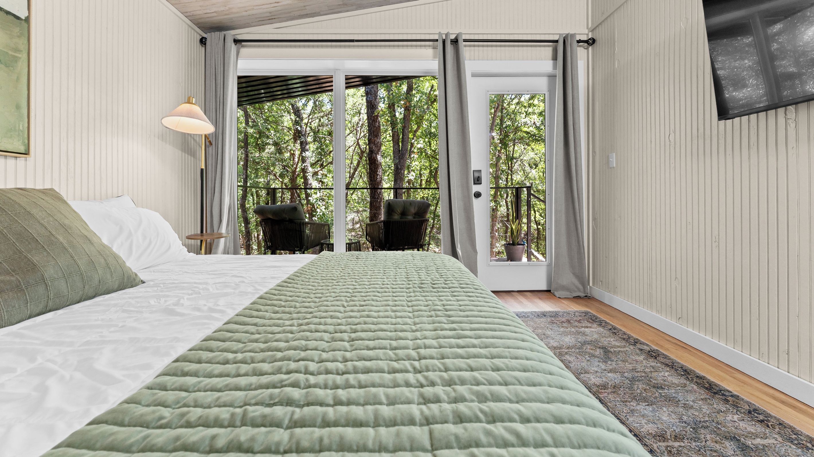Un dormitorio con cama, ventana, una silla y vistas a árboles.