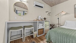 Et værelse med en seng, et skrivebord med to stole, et spejl, aircondition, en lampe og et lille tekøkken.